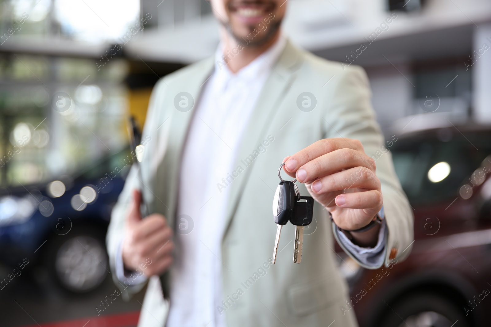 Photo of Salesman with clipboard and car keys in modern auto dealership, closeup