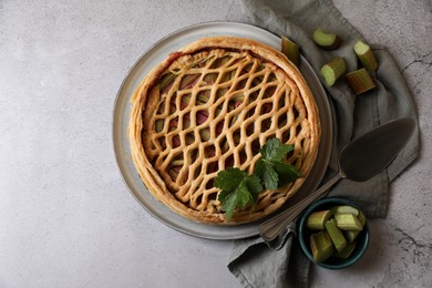 Freshly baked rhubarb pie, cut stalks and cake server on light grey table, flat lay