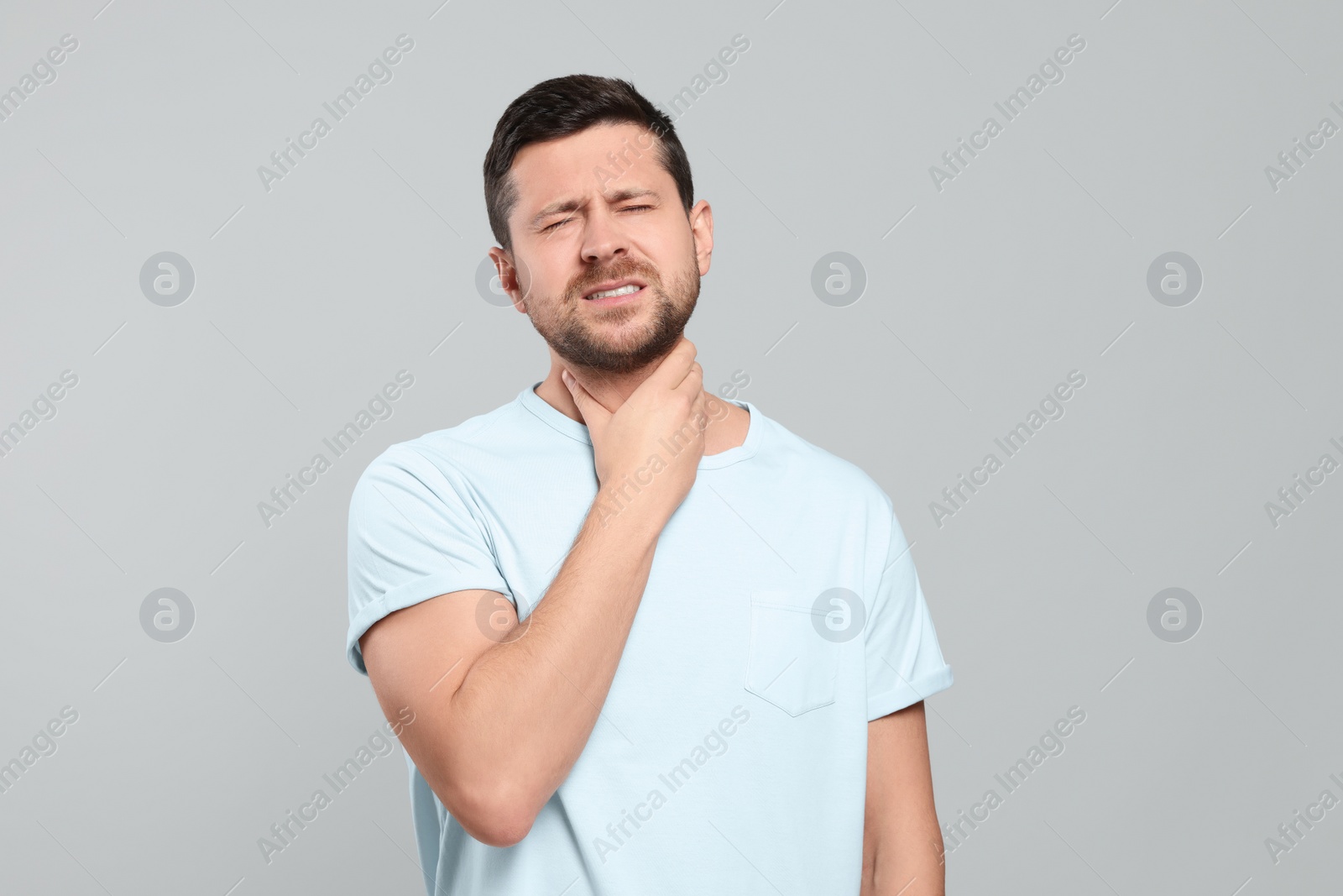 Photo of Man suffering from sore throat on light gray background