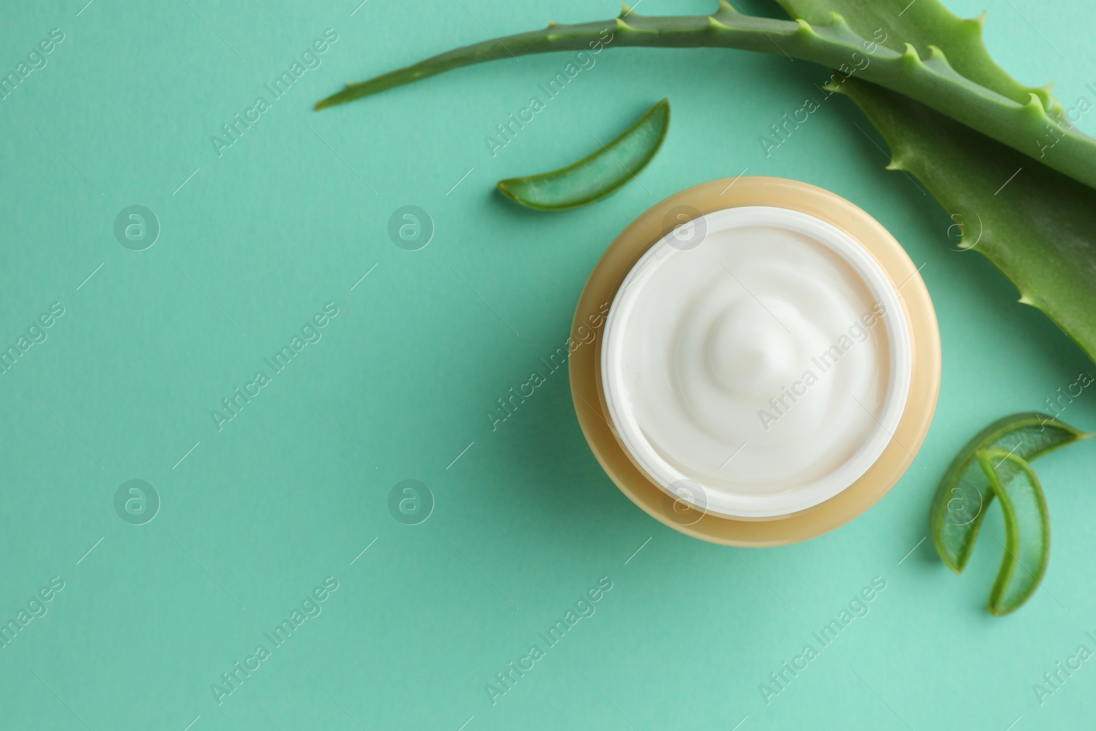 Photo of Jar of natural cream and aloe leaves on green background, flat lay. Space for text