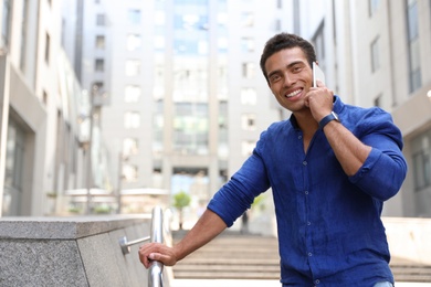 Handsome young African-American man talking on mobile phone outdoors. Space for text