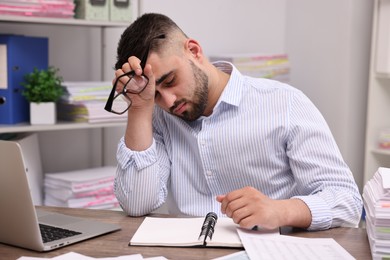 Overwhelmed man with glasses sitting at table in office