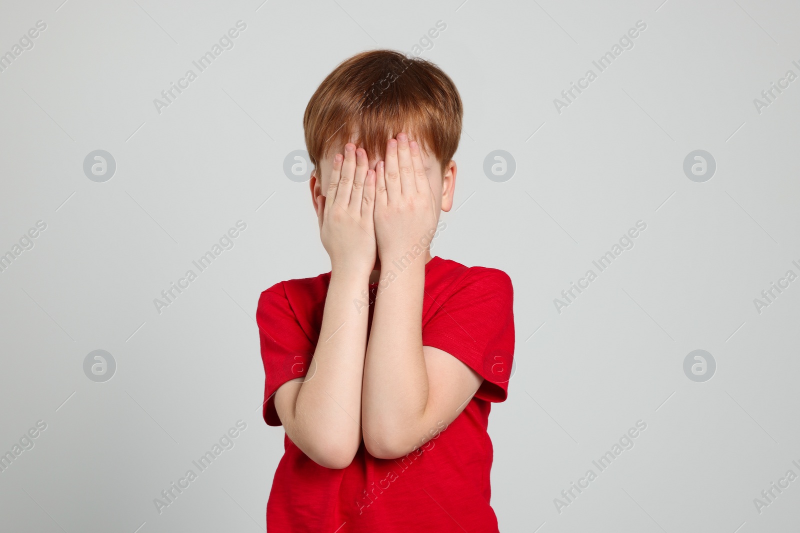 Photo of Boy covering face with hands on light grey background. Children's bullying