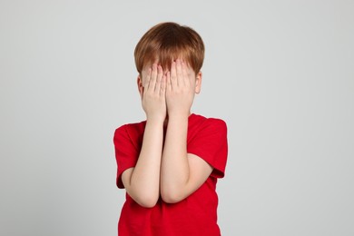 Boy covering face with hands on light grey background. Children's bullying