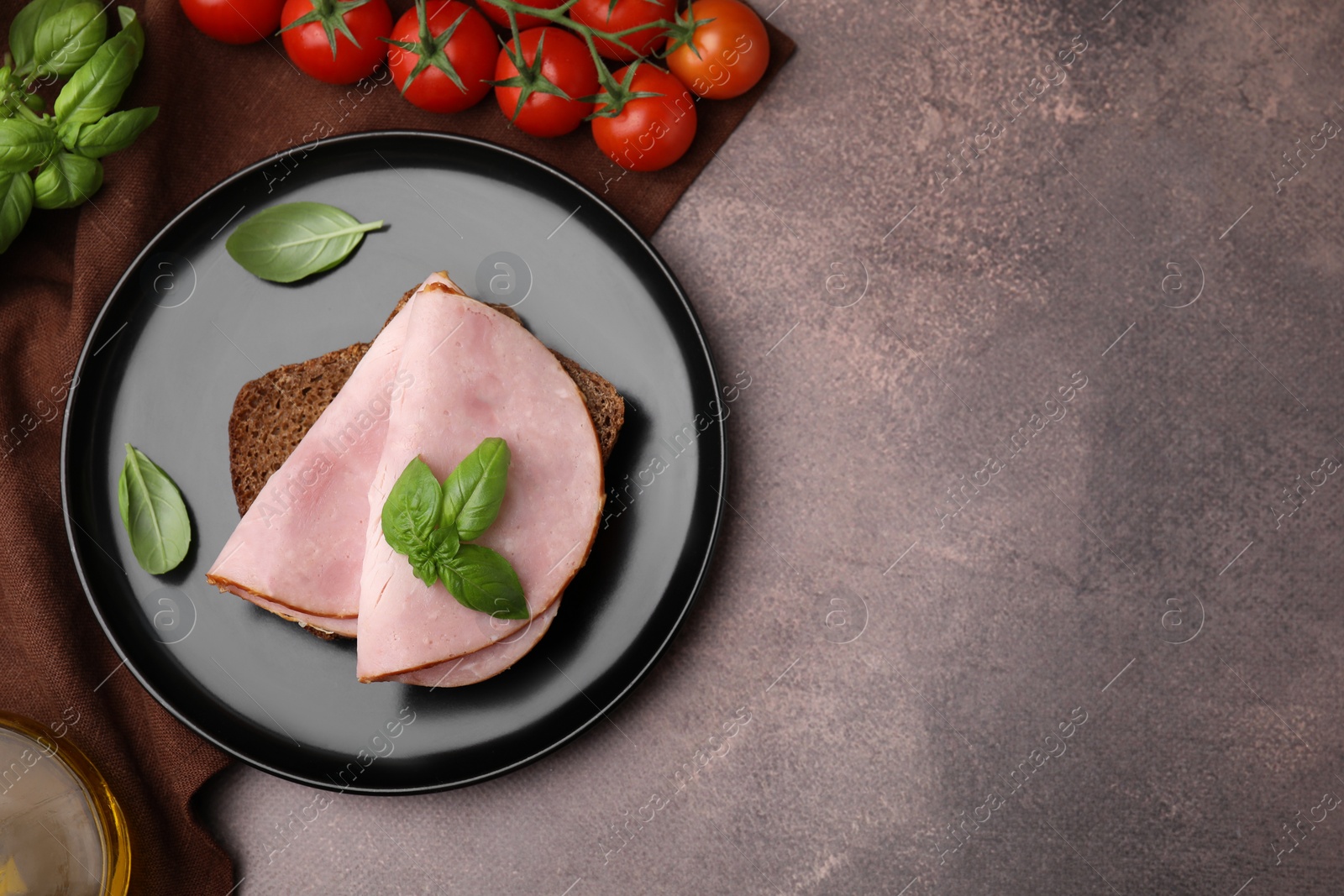 Photo of Delicious sandwich with ham, basil and tomatoes on brown table, flat lay. Space for text