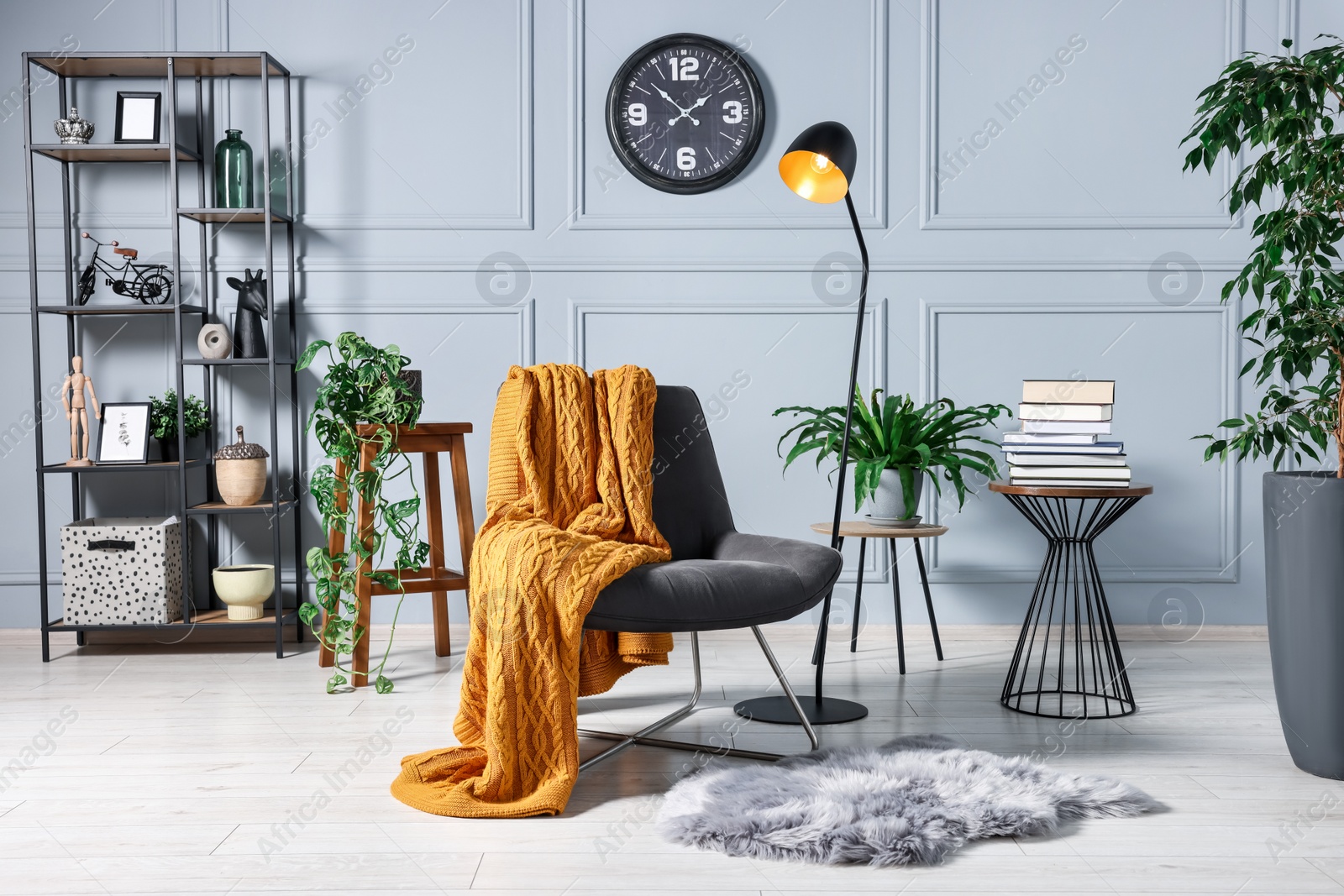 Photo of Comfortable armchair with blanket, houseplants and lamp in room