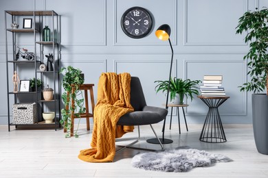 Photo of Comfortable armchair with blanket, houseplants and lamp in room