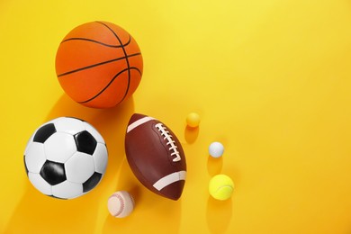 Many different sports balls on yellow background, flat lay. Space for text