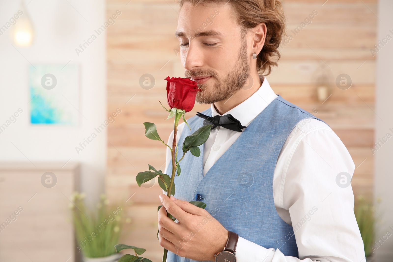 Photo of Handsome man in formal wear holding red rose indoors