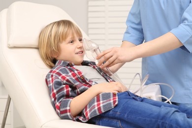 Medical assistant helping sick little boy with nebulizer inhalation at hospital