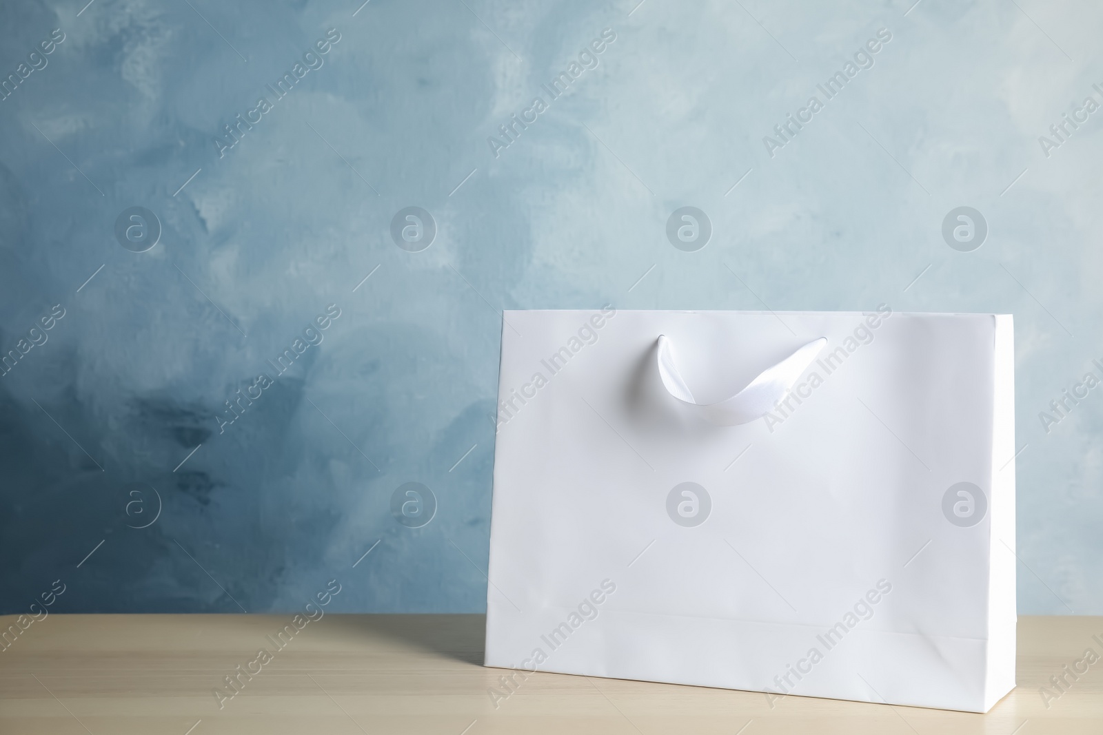 Photo of Paper shopping bag on table against color background. Mock up for design