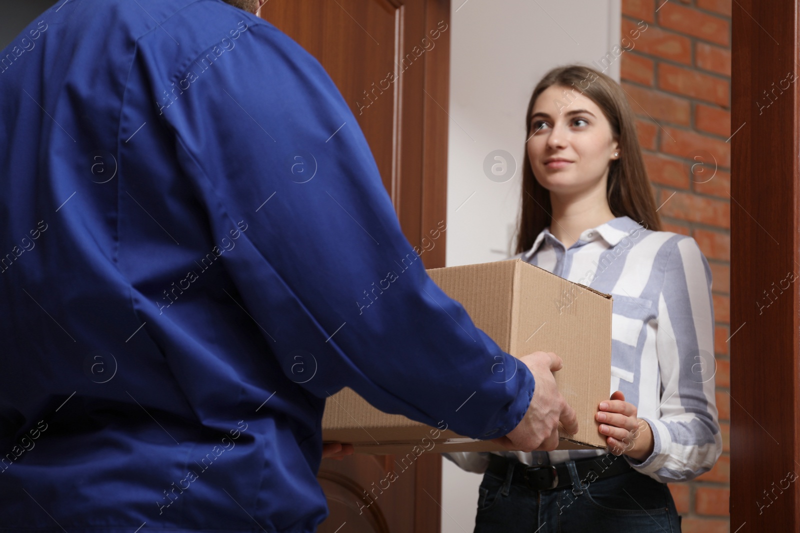 Photo of Young woman receiving parcel from delivery man indoors