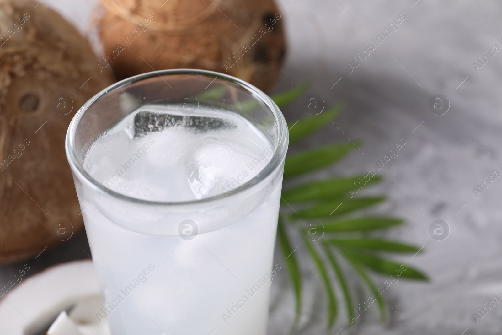 Photo of Glass of coconut water with ice cubes on grey table, closeup. Space for text