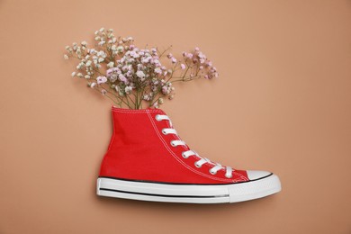 One new stylish red sneaker with gypsophila flowers on beige background, top view