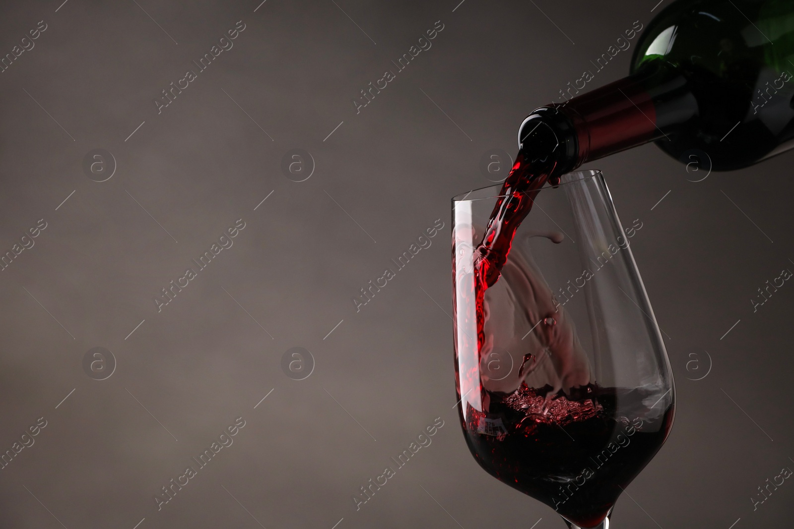 Photo of Pouring tasty red wine from bottle into glass on gray background, closeup. Space for text