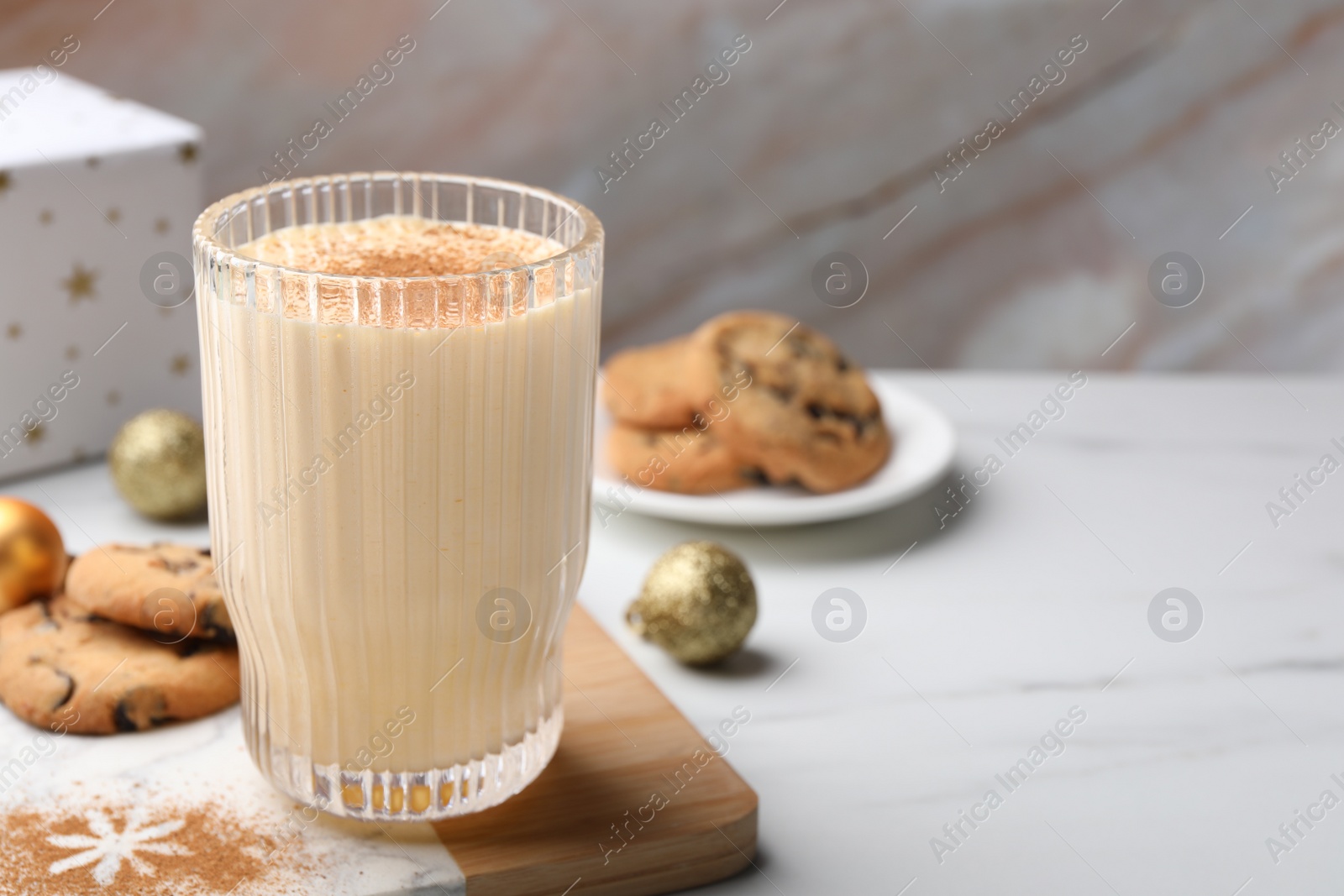 Photo of Glass of delicious eggnog with cinnamon on white table, space for text