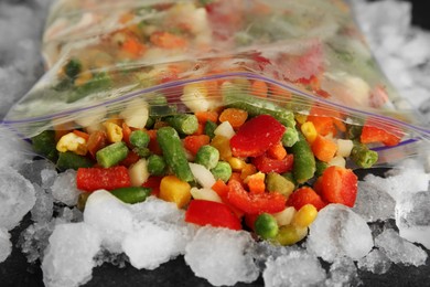 Photo of Zip bag with different frozen vegetables and ice on table, closeup