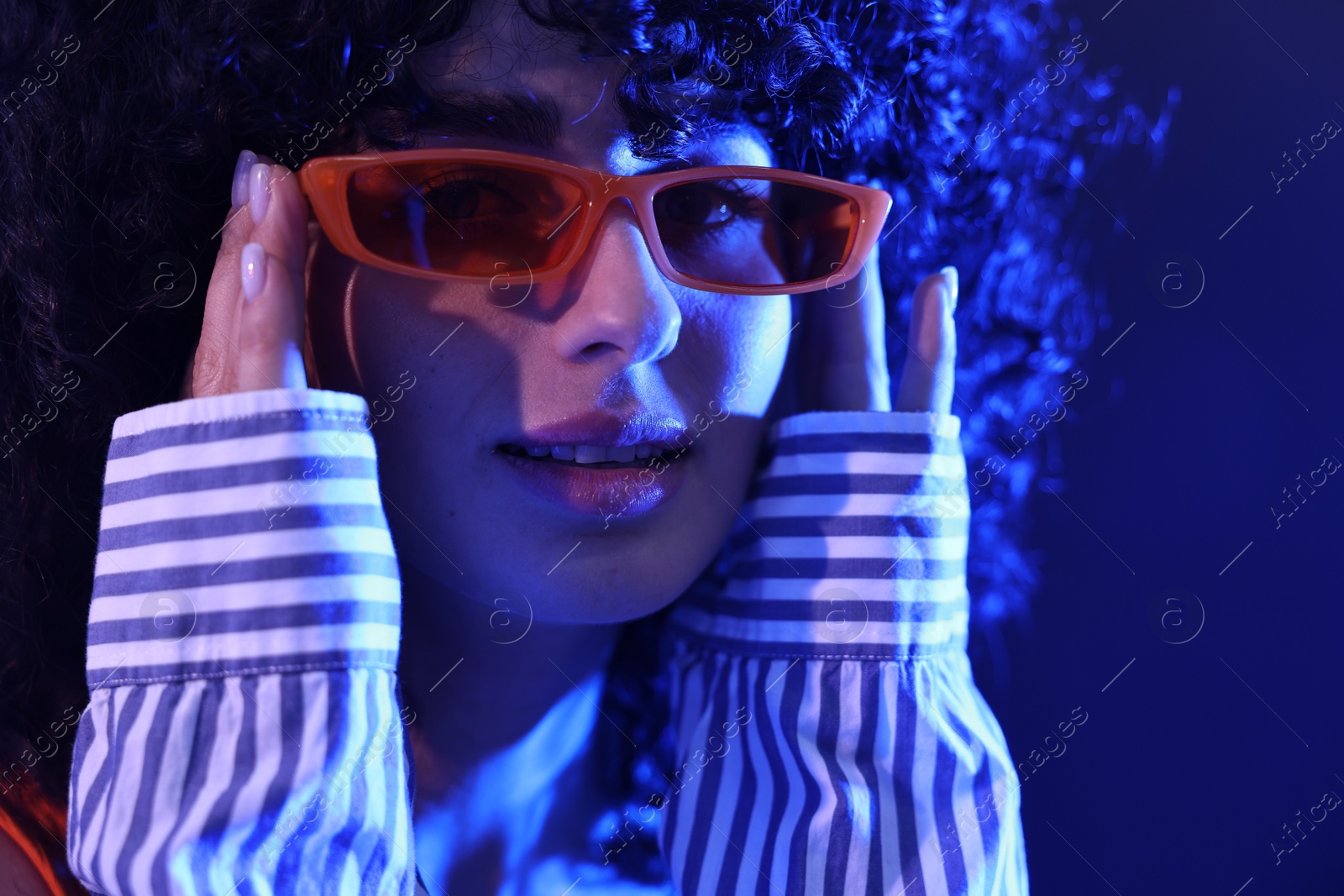 Photo of Beautiful young woman in sunglasses posing on color background in neon lights, closeup