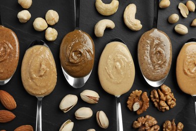 Tasty nut butters in spoons and raw nuts on dark gray table, flat lay