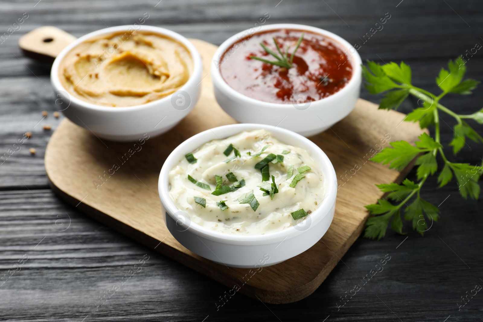 Photo of Different tasty sauces in bowls and parsley on black wooden table, closeup