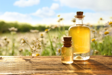 Bottles of chamomile essential oil on wooden table in field. Space for text