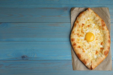 Photo of Fresh homemade khachapuri with cheese and egg on light blue wooden table, top view. Space for text