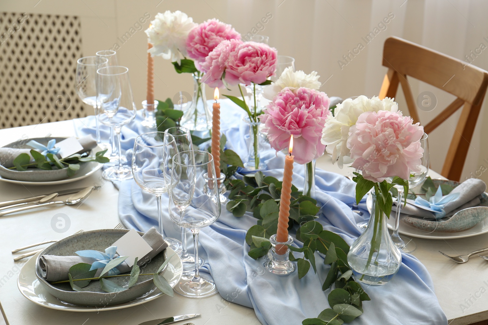 Photo of Beautiful table setting. Plates with greeting cards, napkins and branches near glasses, peonies, burning candles and cutlery on table indoors