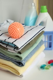 Photo of Orange dryer ball on stacked clean clothes near laundry detergents