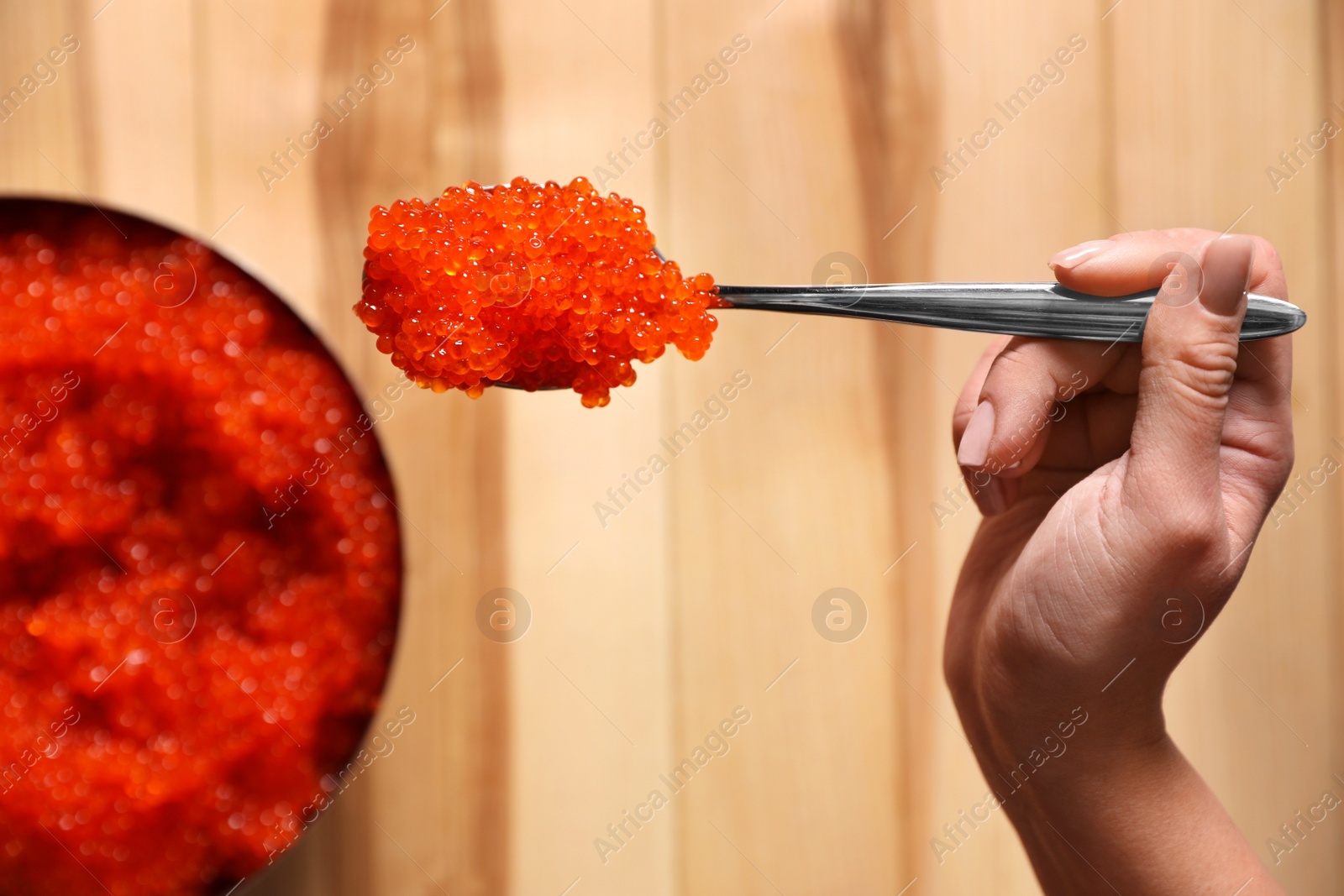 Photo of Woman holding spoon with fresh red caviar at wooden table, top view