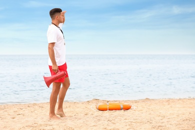 Photo of Handsome male lifeguard with megaphone at sandy beach