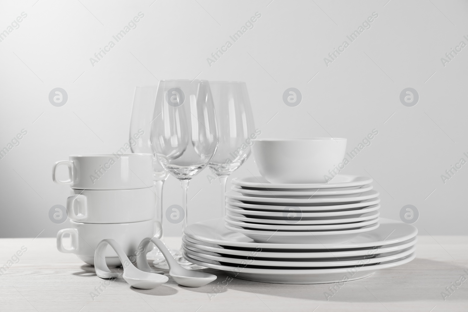 Photo of Set of clean dishware and glasses on white wooden table against light background