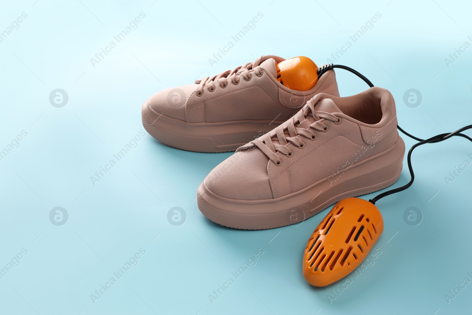 Photo of Pair of stylish shoes with modern electric footwear dryer on light blue background. Space for text