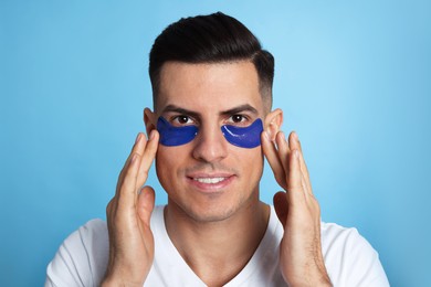 Photo of Man applying under eye patches on light blue background
