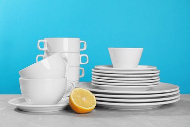 Photo of Clean tableware and half of lemon on grey table against light blue background