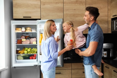 Happy family with bottle of juice near refrigerator in kitchen
