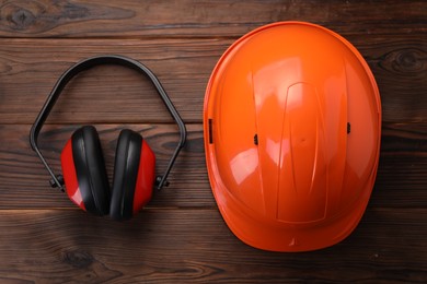 Safety equipment. Hard hat and protective headphones on wooden background, flat lay
