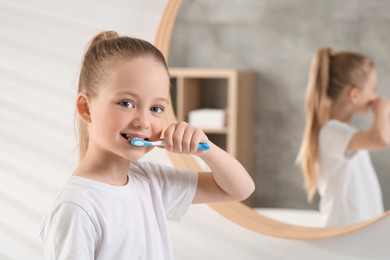 Photo of Cute little girl brushing her teeth with plastic toothbrush in bathroom, space for text