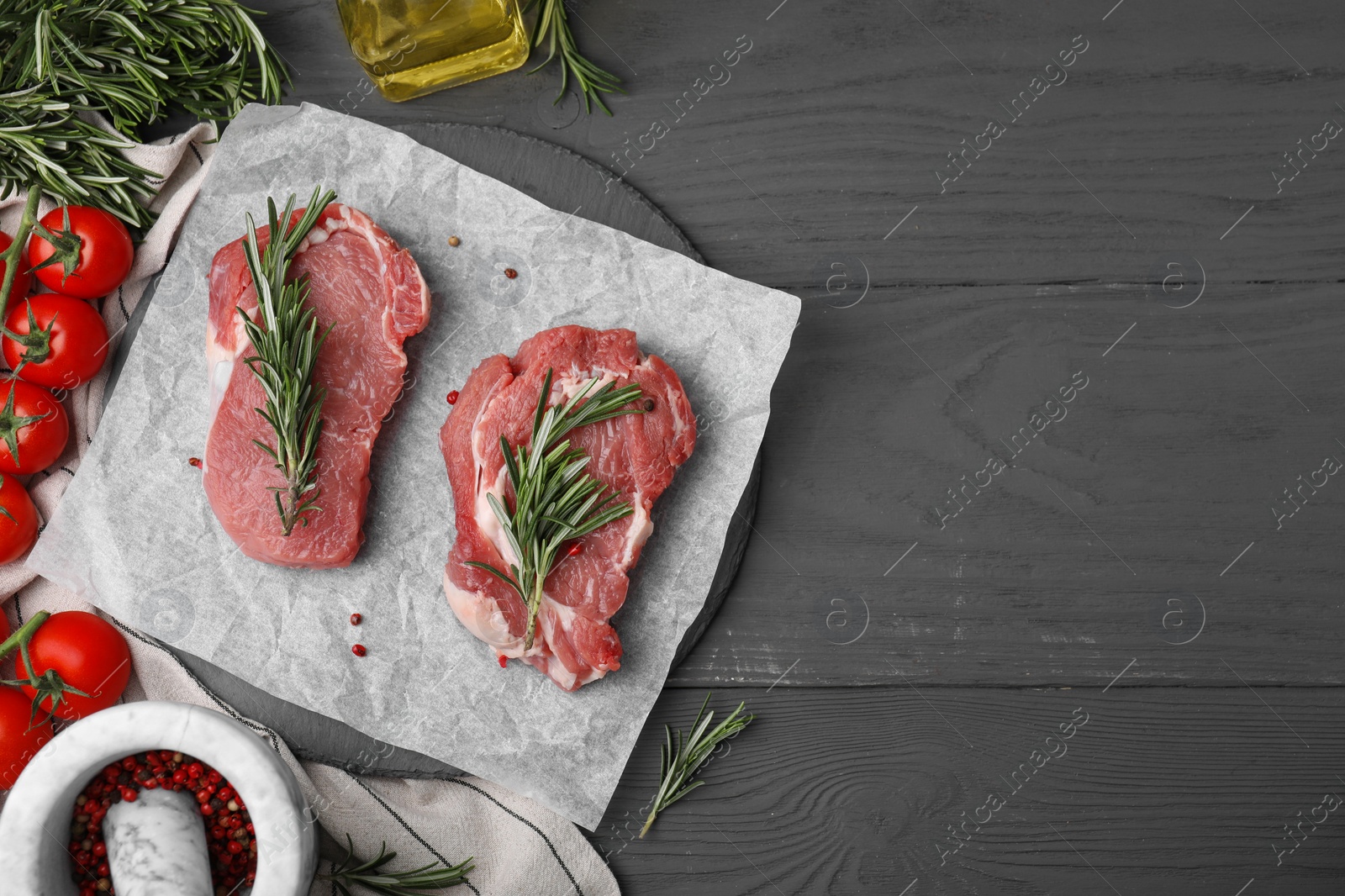 Photo of Fresh raw meat with rosemary, tomatoes and spices on grey wooden table, flat lay. Space for text