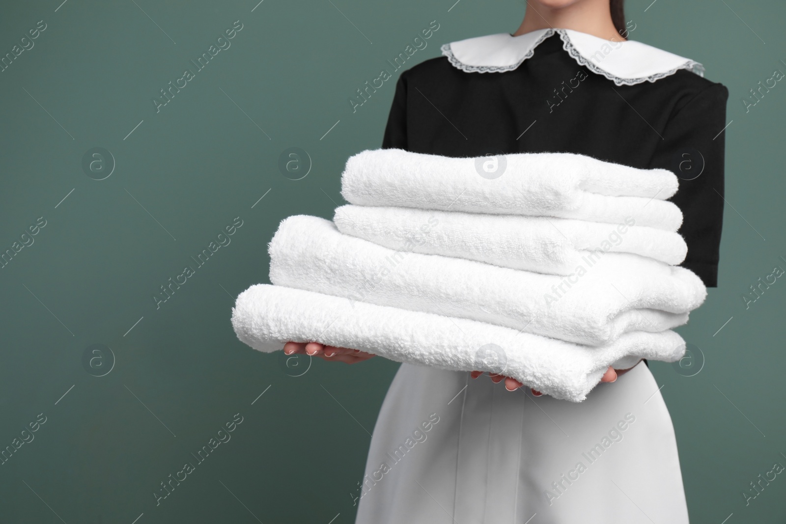 Photo of Young chambermaid with stack of clean towels on color background