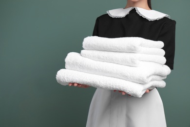 Young chambermaid with stack of clean towels on color background