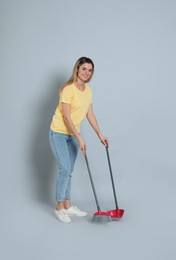 Young woman with broom and dustpan on grey background