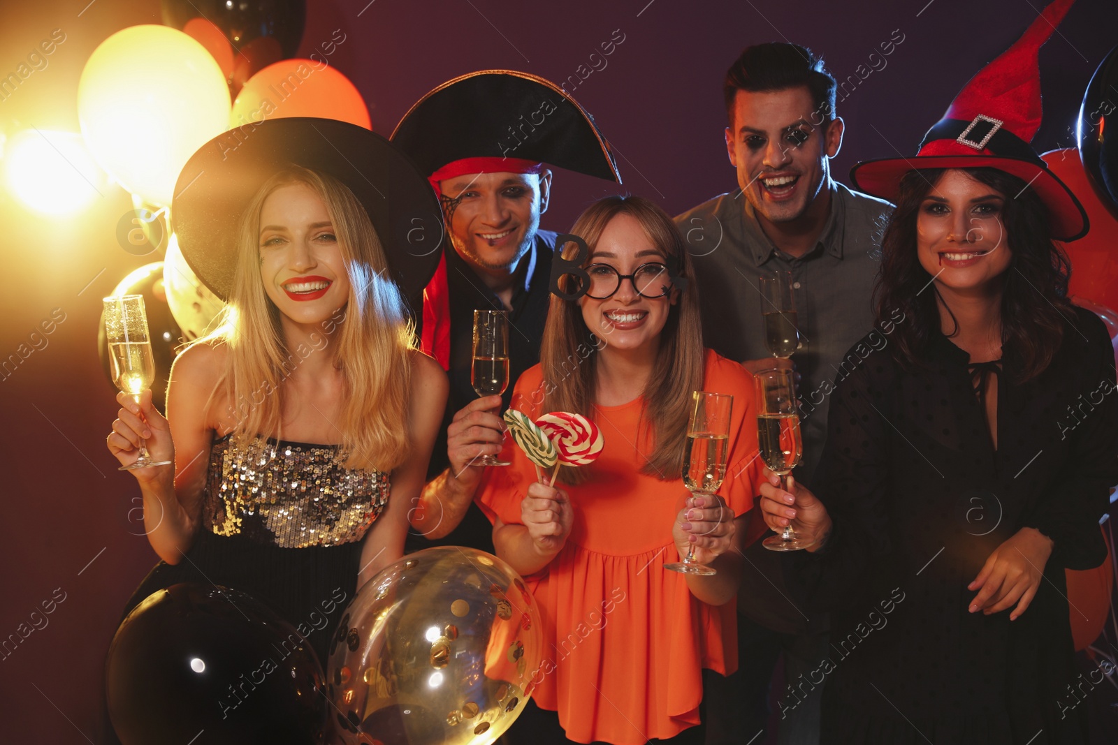 Photo of Happy friends in costumes enjoying Halloween party on dark background