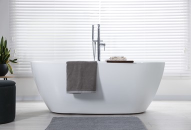 Photo of Stylish bathroom interior with ceramic tub, terry towels and houseplant