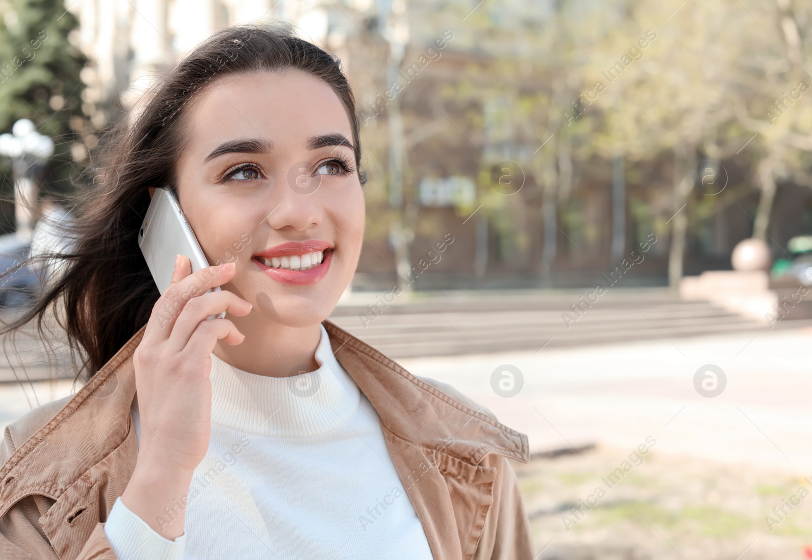 Photo of Young woman talking by phone outdoors on sunny day