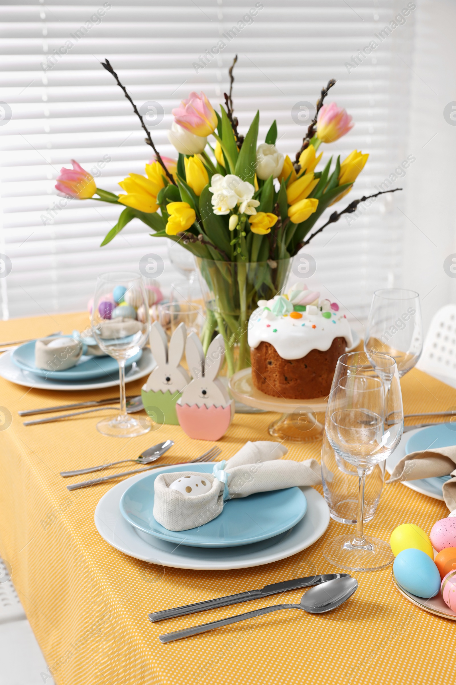 Photo of Festive table setting with painted eggs, traditional Easter cake and vase of tulips