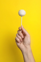 Photo of Woman holding sweet cake pop on yellow background, closeup