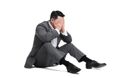 Tired businessman in suit sitting on white background