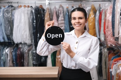 Dry-cleaning service. Happy worker holding Open sign indoors, space for text