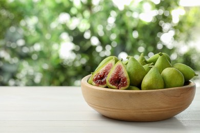 Photo of Cut and whole fresh green figs on white wooden table against blurred background, space for text