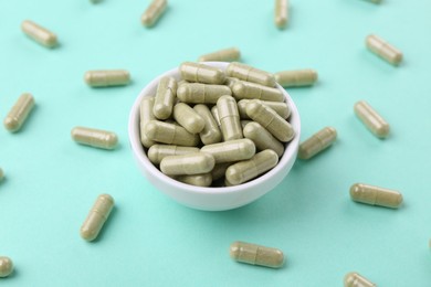 Bowl with vitamin capsules on turquoise background, closeup